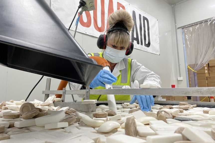 A worker cleaning soap bars with a vaccum cleaner type machine at the Soap Aid facility