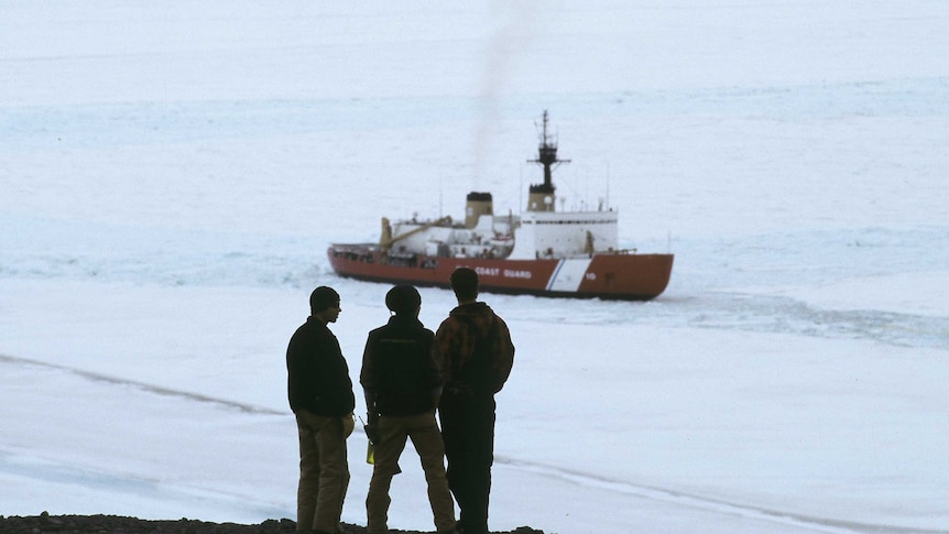 Three men watch the US Coast Guard plunge through ice.