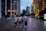 A group of Asian people stand together in the middle of shopping strip in Shanghai to take a selfie