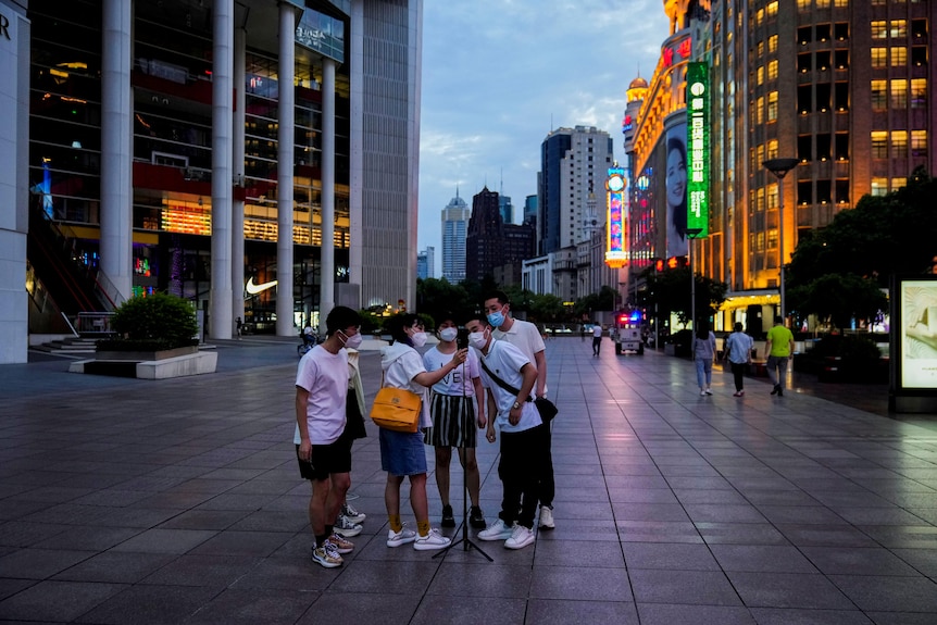 A group of Asian people stand together in the middle of shopping strip in Shanghai to take a selfie
