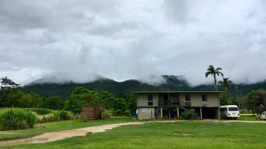 A house on the right hand side of the photo looks small when surrounded by misty skies and mountains and vivid green grass.