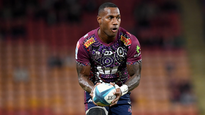 A male Queensland Reds player holds the ball in both hands during a Super Rugby Pacific match.