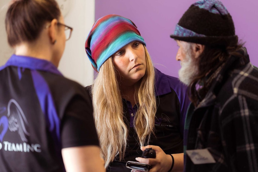 Dee Freitag stands listening intently to a man as he talks with another woman in the foreground of the picture.