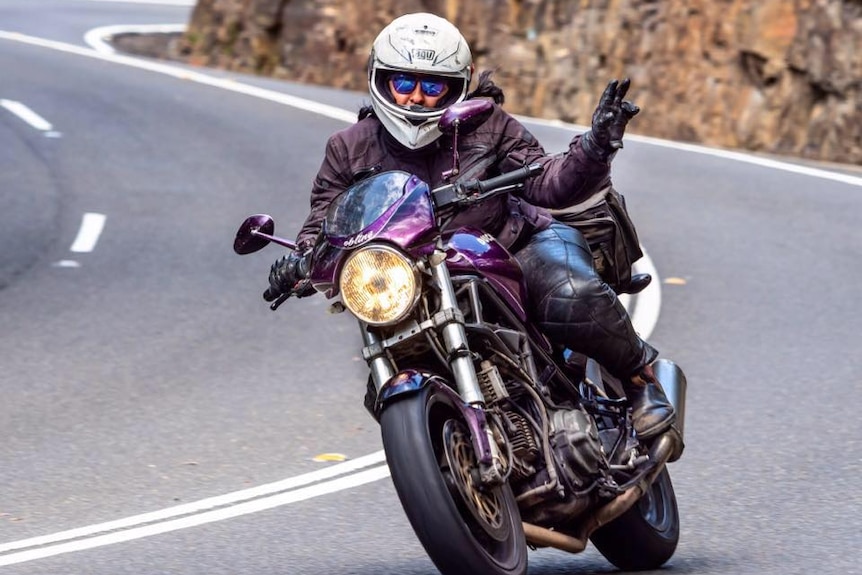 A woman wearing a purple jacket and riding a purple motorcycle on the road