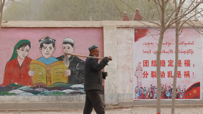 A farmer walks past propaganda depicting ethnic minority residents reading the Chinese constitution
