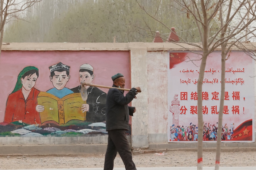 A farmer walks past propaganda depicting ethnic minority residents reading the Chinese constitution