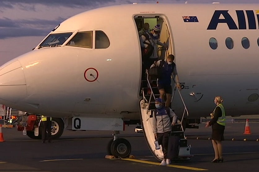 people in masks getting off a plane on a runway