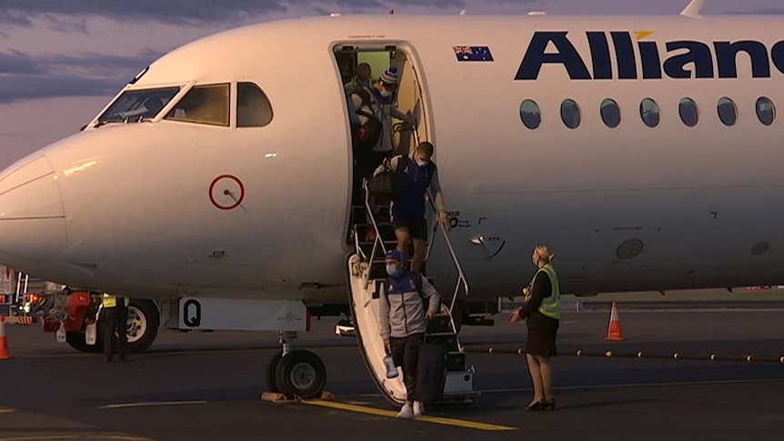 people in masks getting off a plane on a runway