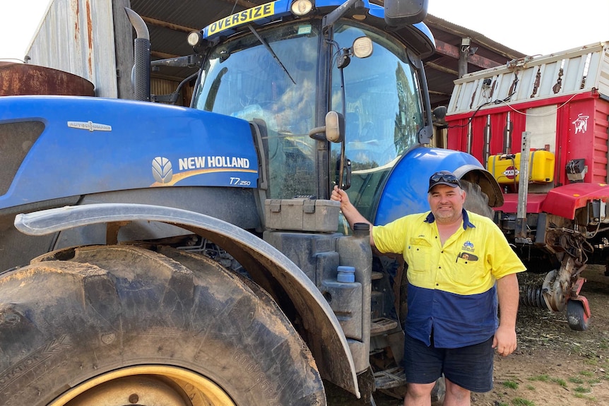 A man wearing a high vis shirt and hat stands next to a large blue tractor.