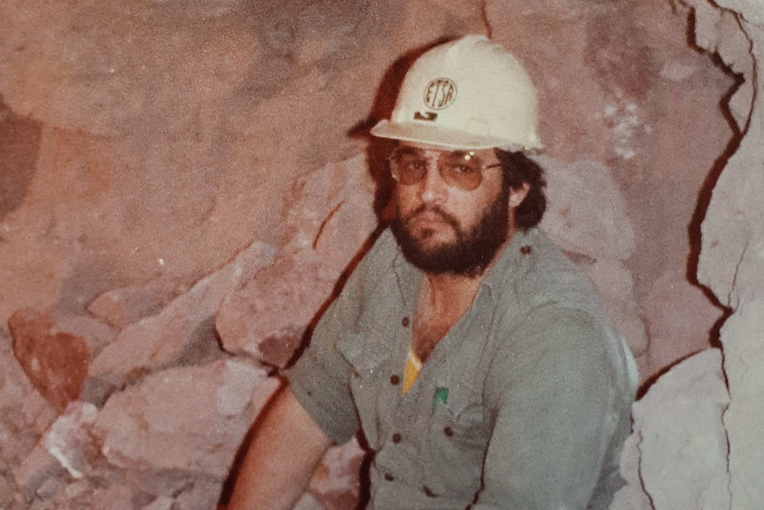 A man in jeans and a hard hat underground in a mine.