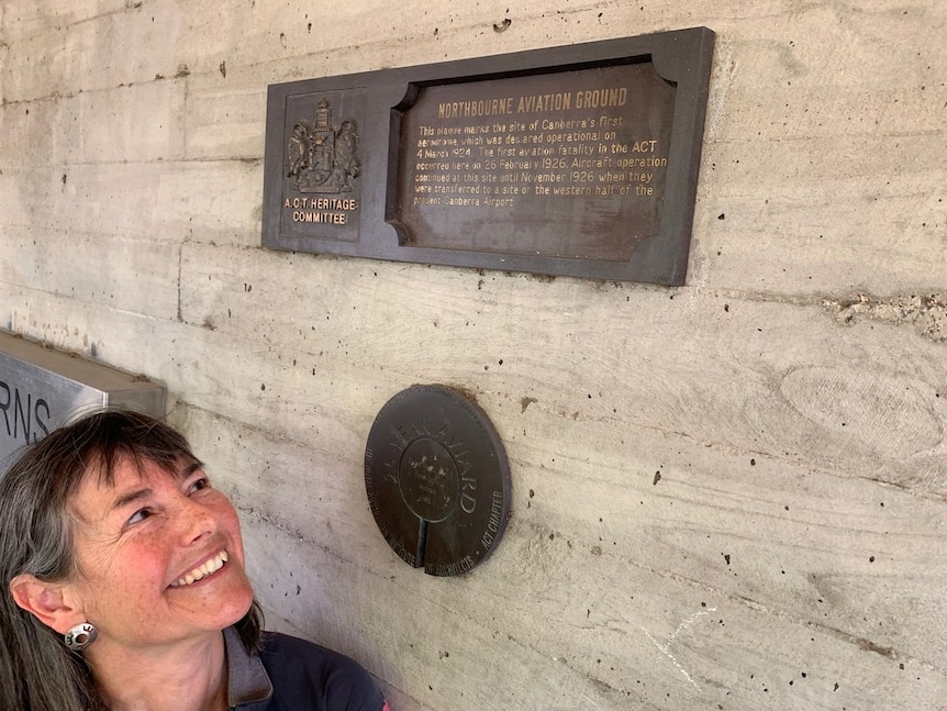 A woman looks up at a plaque on a building.