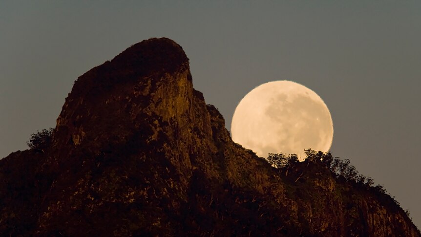 The moon rises over the peak of a rocky mountain