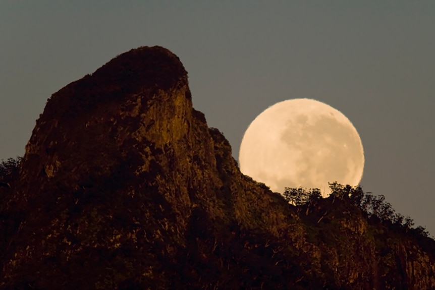 The moon rises behind a mountain peak