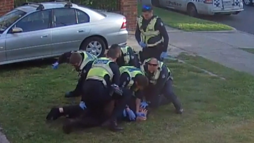 A number of police pin John down on his front lawn.