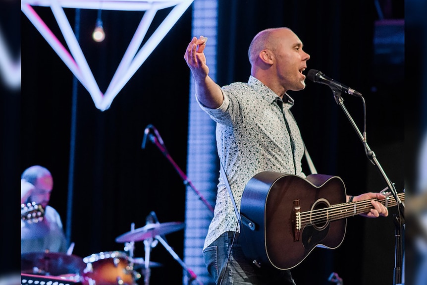 A man plays a guitar and sings in a church.