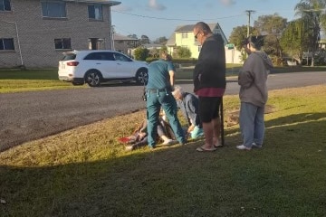 Two women, a man and a paramedic attend to a woman lying on the ground.