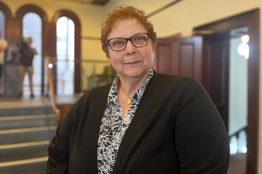 A woman wearing glasses looks at the camera