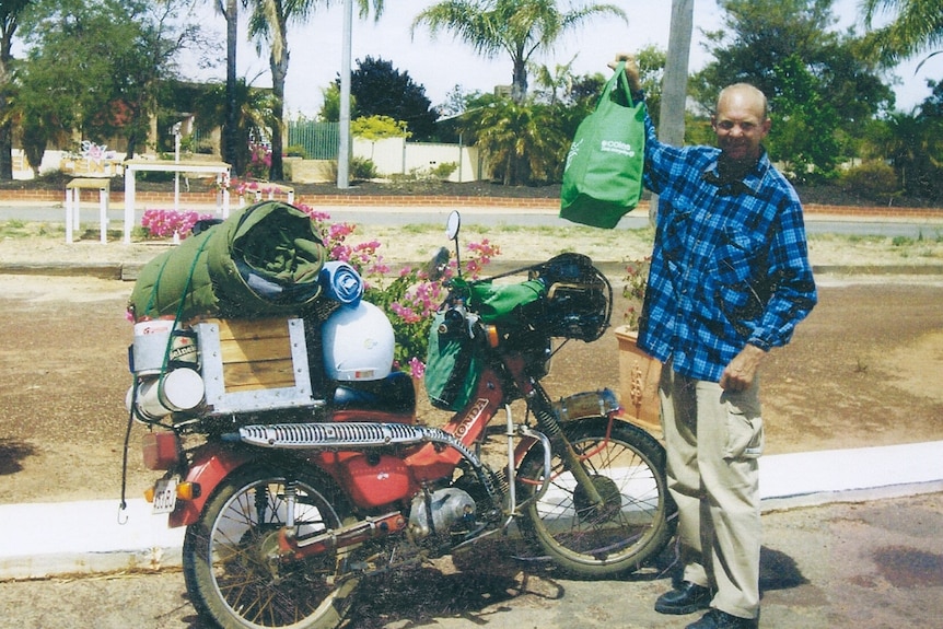 Man standing nearly postie bike with box, swag and helmet on the bag, man holding up shopping bag and smiing 