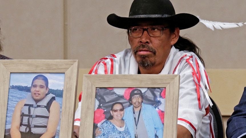 A man sitting in front of two framed photos, one with a child and one with a woman and man