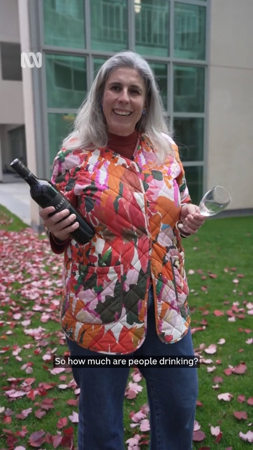 A middle-aged woman holds a wine bottle in one hand and a wine glass in the other