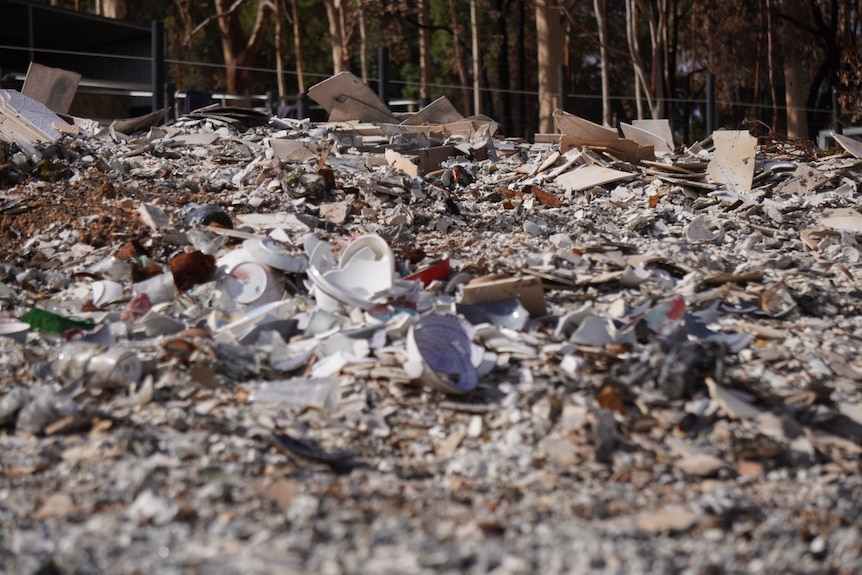 A close-up pile of rubble from a fire-destroyed property with burnt gum trees in the background.