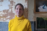 Anna Reece standing in front of a peeling wall in with paintings to her right.