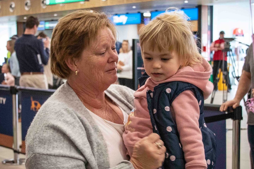 A woman tears up as she holds a toddler in the arrivals section of the Hobart airport