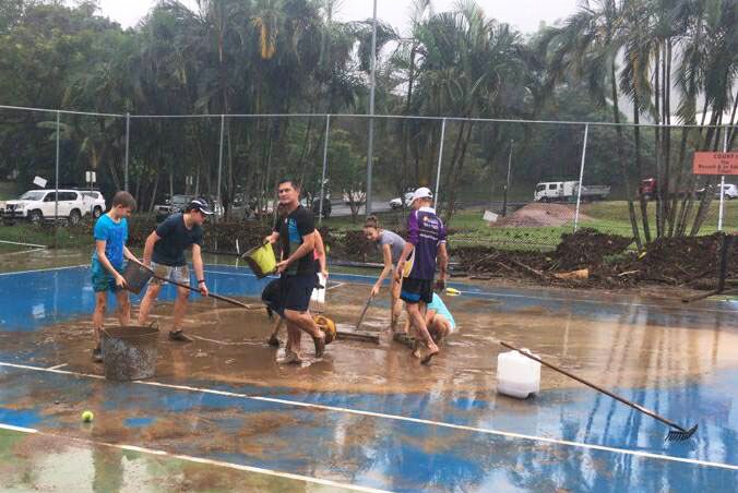 People clean up debris on a tennis court at the Redlynch Valley Tennis Club in Cairns on March 28, 2018, after floods.