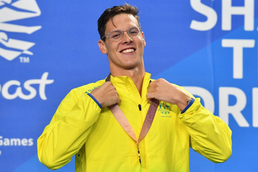Mitch Larkin stands on the podium, smiling and wearing a Gold Medal.