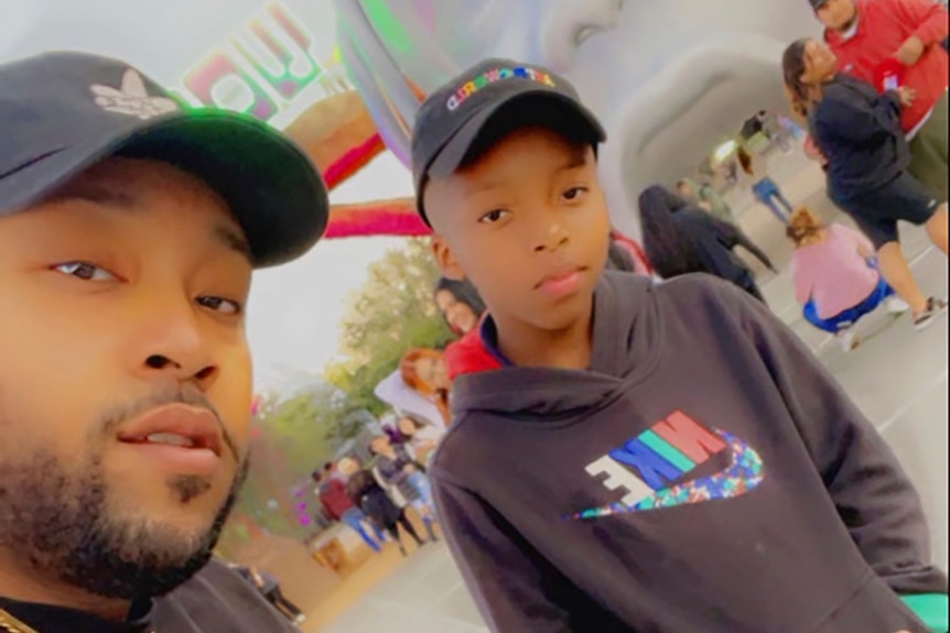 A young African American man poses with a young black boy at an outdoor music concert entrance