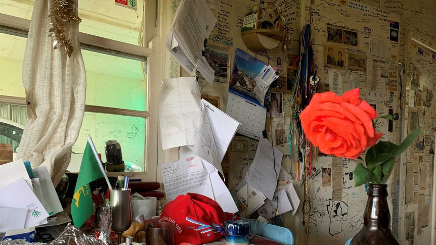 Ben Buckley's kitchen table, covered in books, a flag, notes and a wall lined with with notes and pictures.