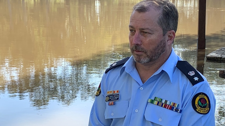 Man in blue shirt stand in front of a flooded BBQ shed