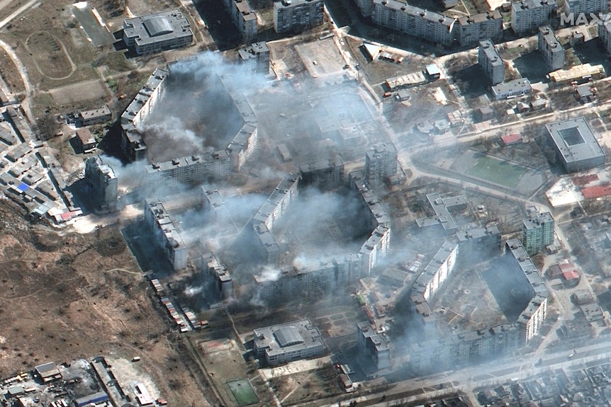 A satellite aerial image of a number of buildings in the city of Mariupol with smoke billowing from them
