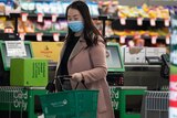 a woman wearing a mask carrying a shopping basket inside a grocery store