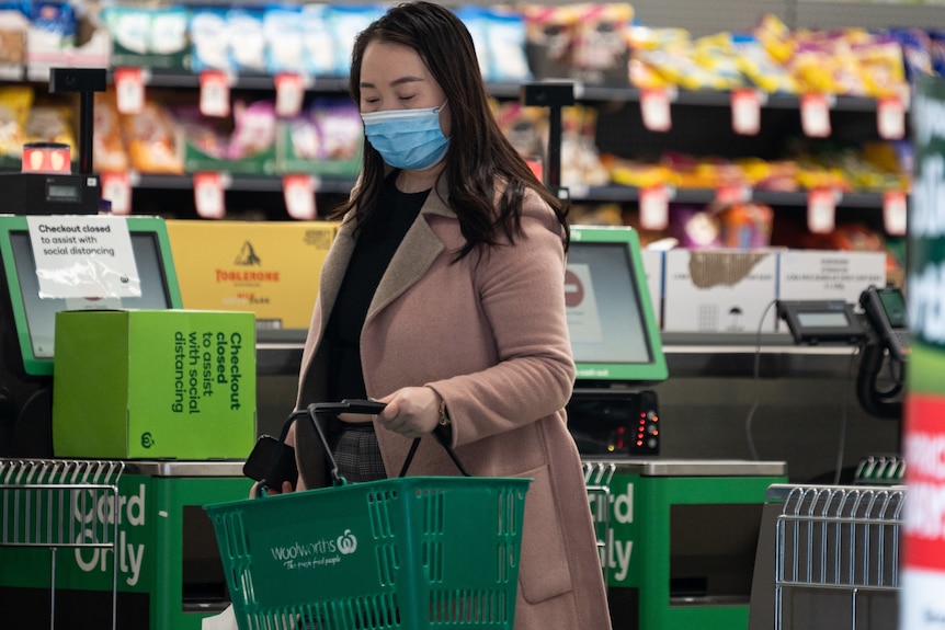 a woman wearing a mask carrying a shopping basket inside a grocery store