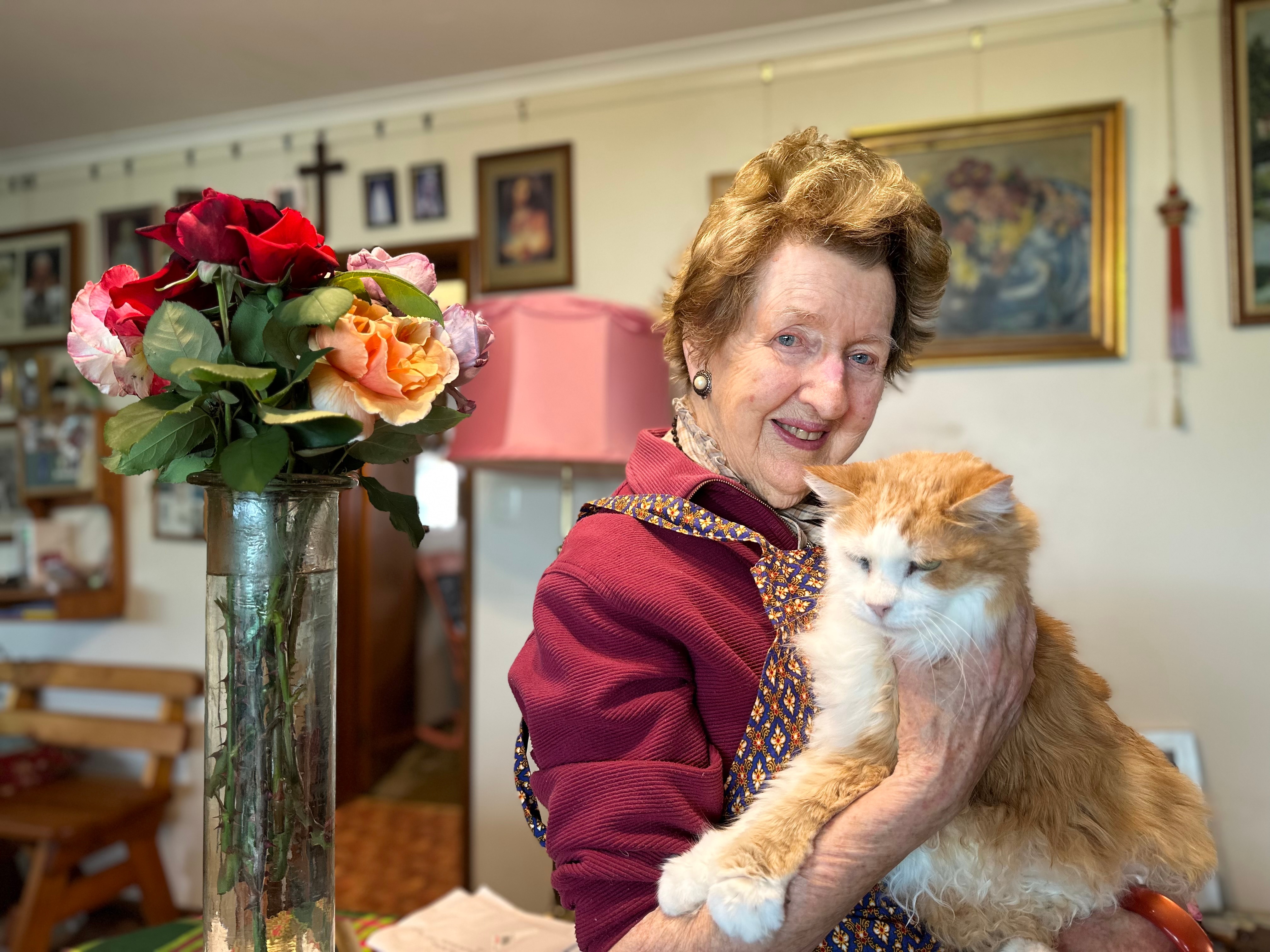 A woman with a cat next to a vase of roses.