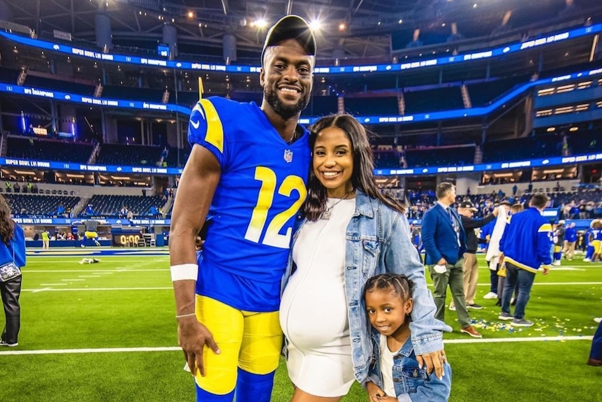 Los Angeles Rams player Van Jefferson (left) stands with pregnant wife and their daughter on a football field after an NFL game.