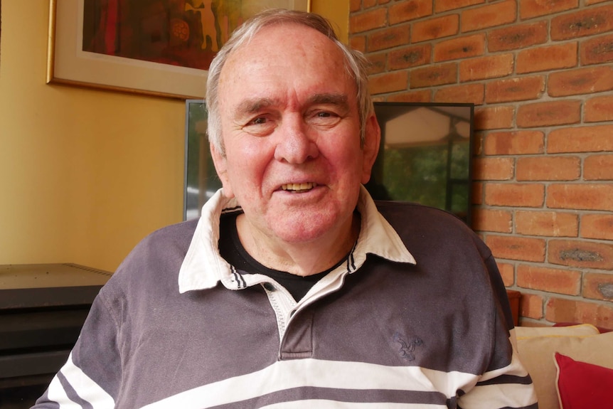 A man smiles at the camera, wearing a blue and white striped jumper.