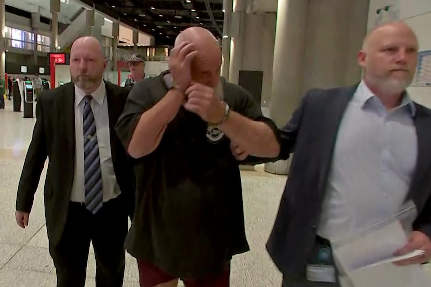 A man in handcuffs tries to shield his face from cameras