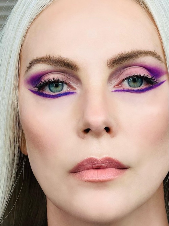 A woman with vivid eye make-up and silver hair stares into the camera