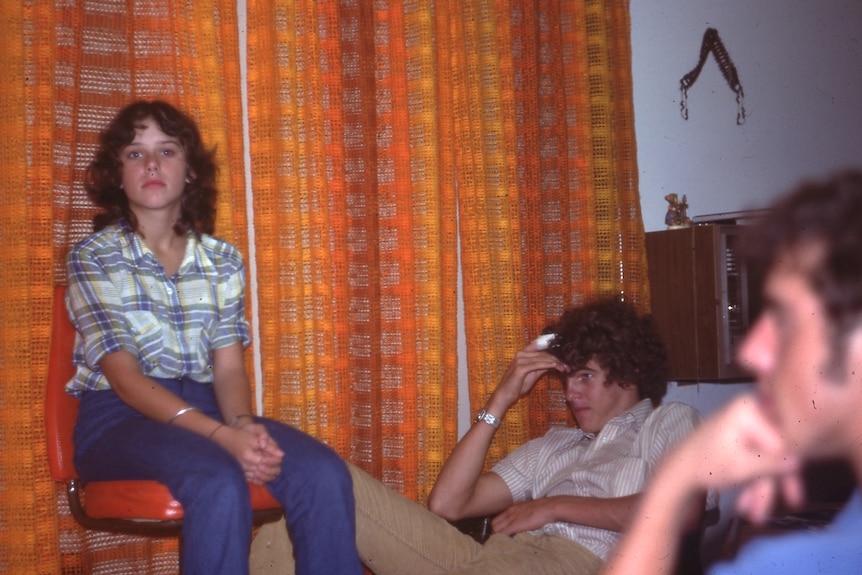 A 1970s slide of three young people sitting in front of an orange and yellow curtain