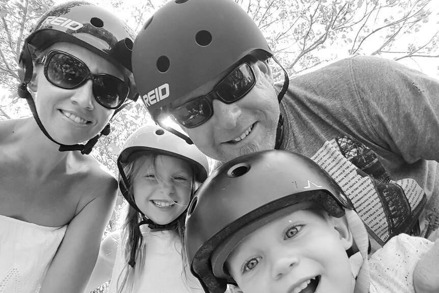 Black and white photo of Aaron Cox and his wife Bindi and two children wearing helmets.