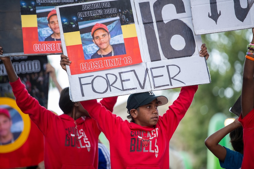A young Indigenous boy holding a Forever 16 sign at a rally