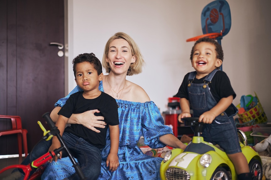 Géraldine sits with her two children amongst their toys