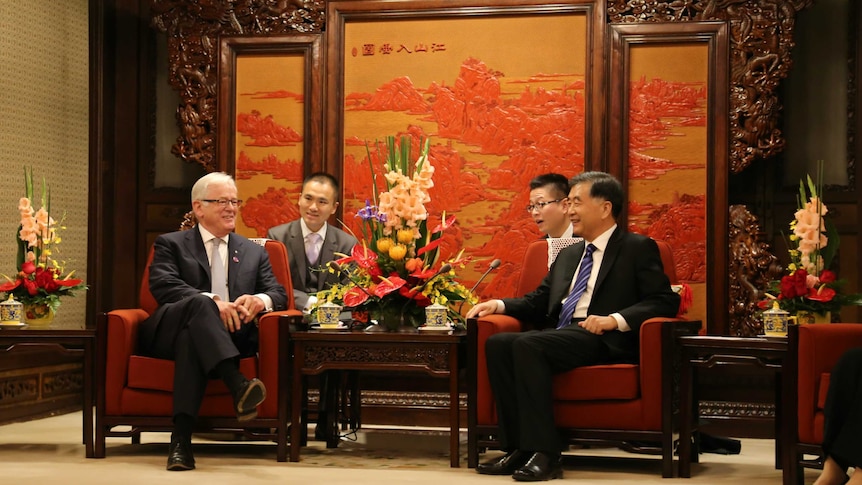 Andrew Robb and Rex Chen sitting together in front of a Chinese facade with two other men