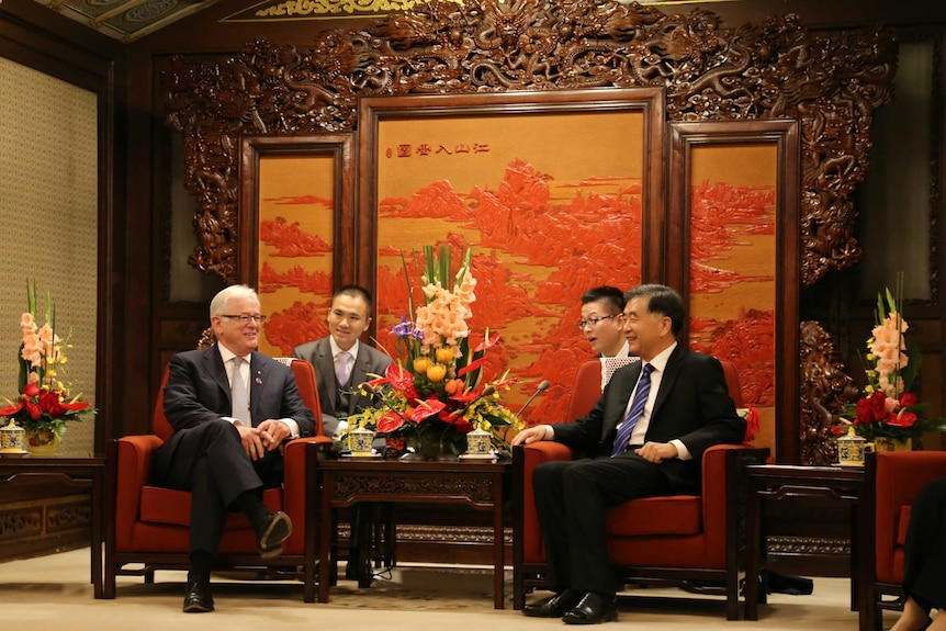 Andrew Robb and Rex Chen sitting together in front of a Chinese facade with two other men