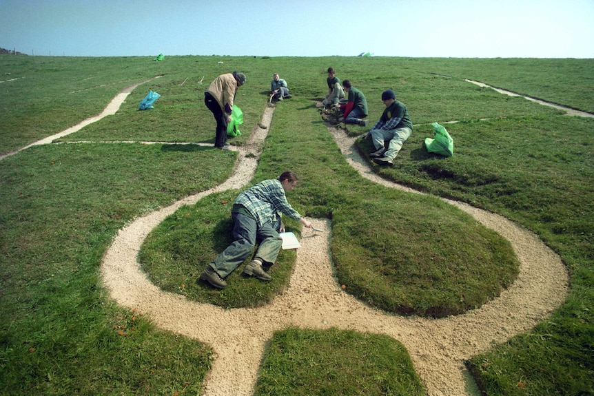 Wide angle shot of a group of people working on a sand outline of a giant figure on a hillside.