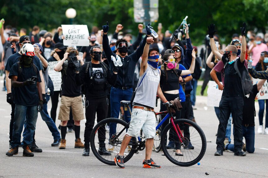 Protesters on the street, most wearing masks, with their hands in the air.