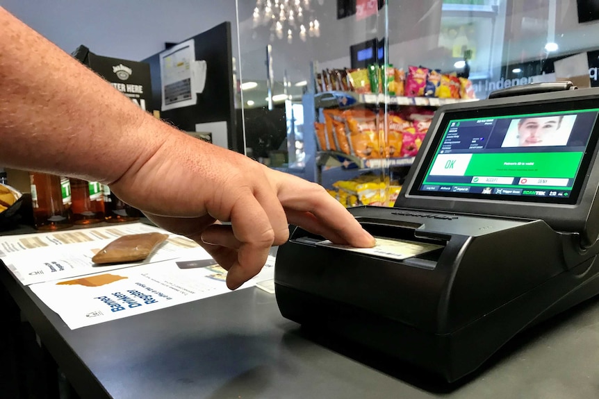 Hand scanning an ID card on a shop counter.