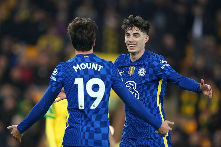 A Premier League footballer smiles as he runs in with arms outstretched to hug a teammate after scoring a goal.